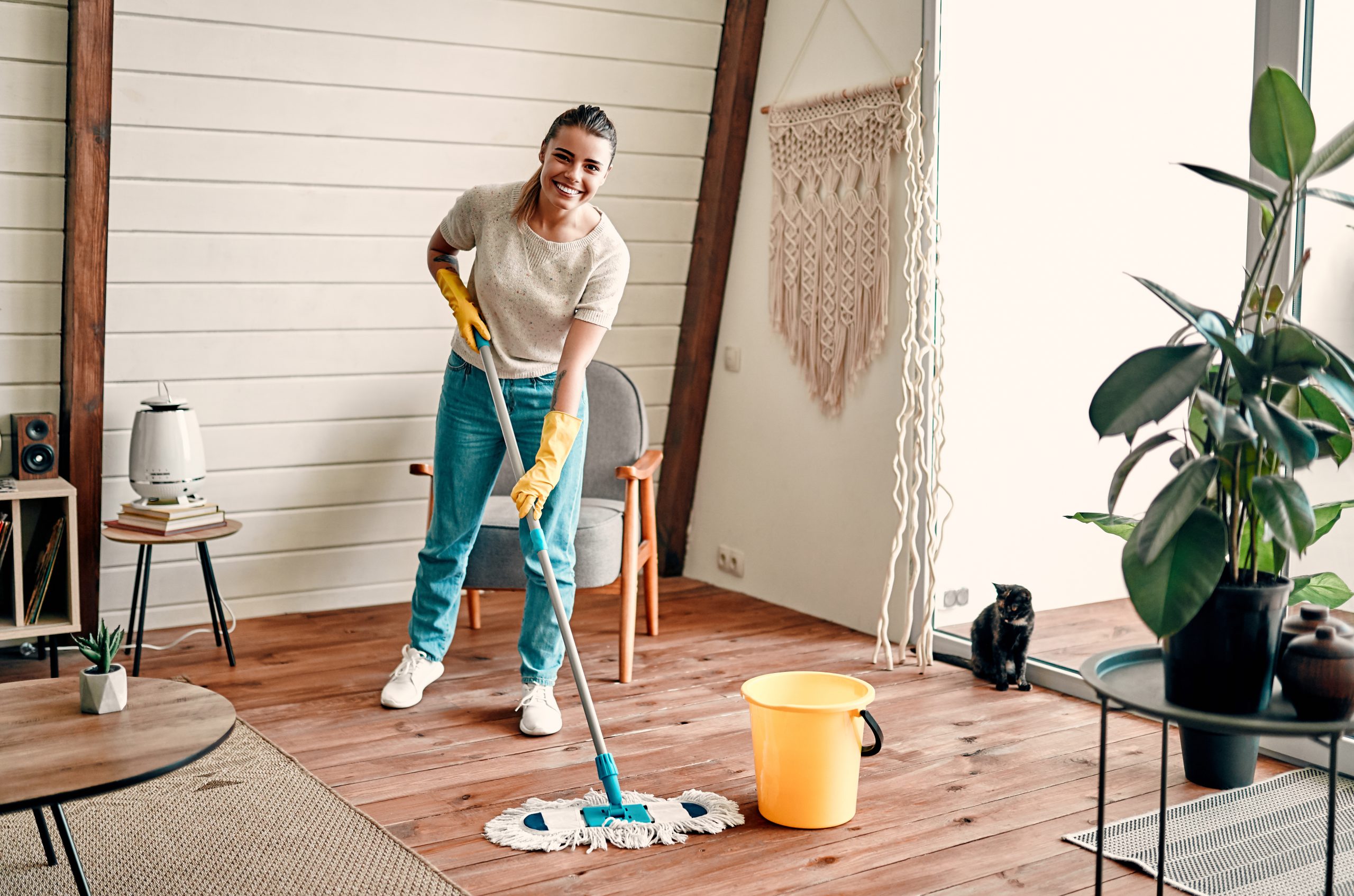 Woman cleaning oak wood flooring in a Catford home after expert wood floor sanding, smiling with mop and gloves.