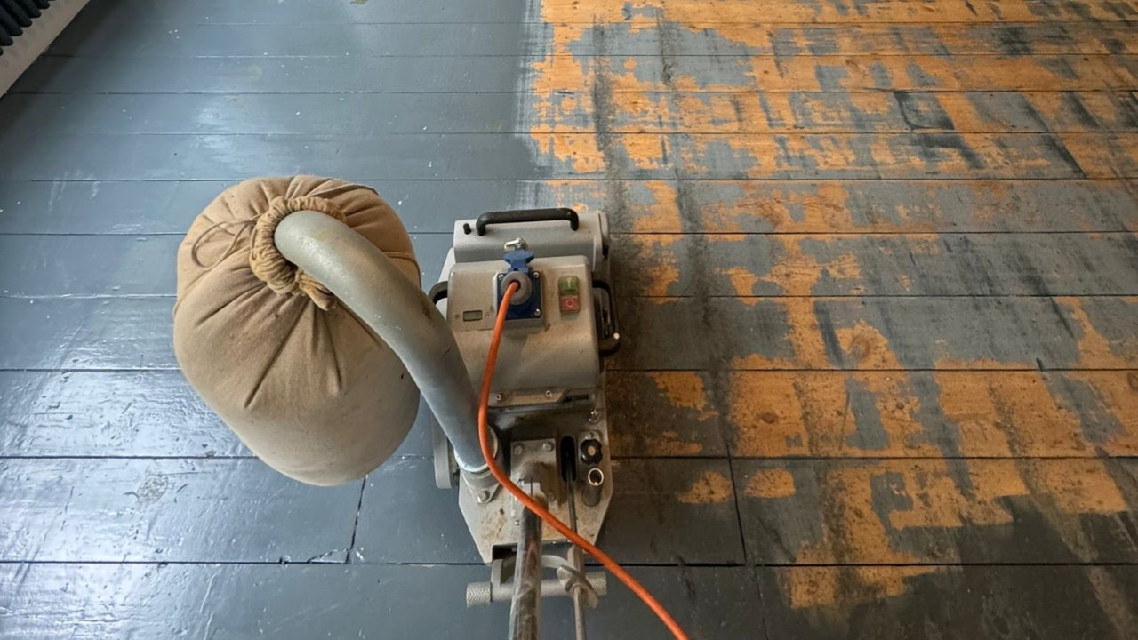 A belt sander revealing natural pine boards beneath dark paint during expert wood floor sanding in Catford.