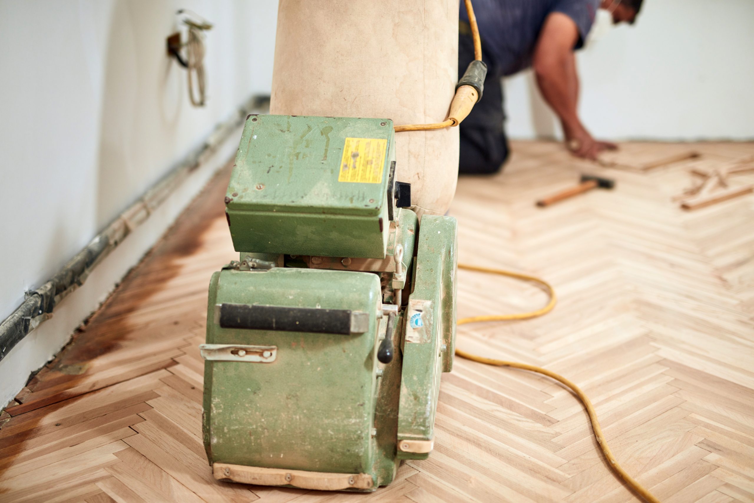Floor sanding machine in use on herringbone parquet flooring with technician working in background during a Professional Wood Floor Sanding project in Catford.