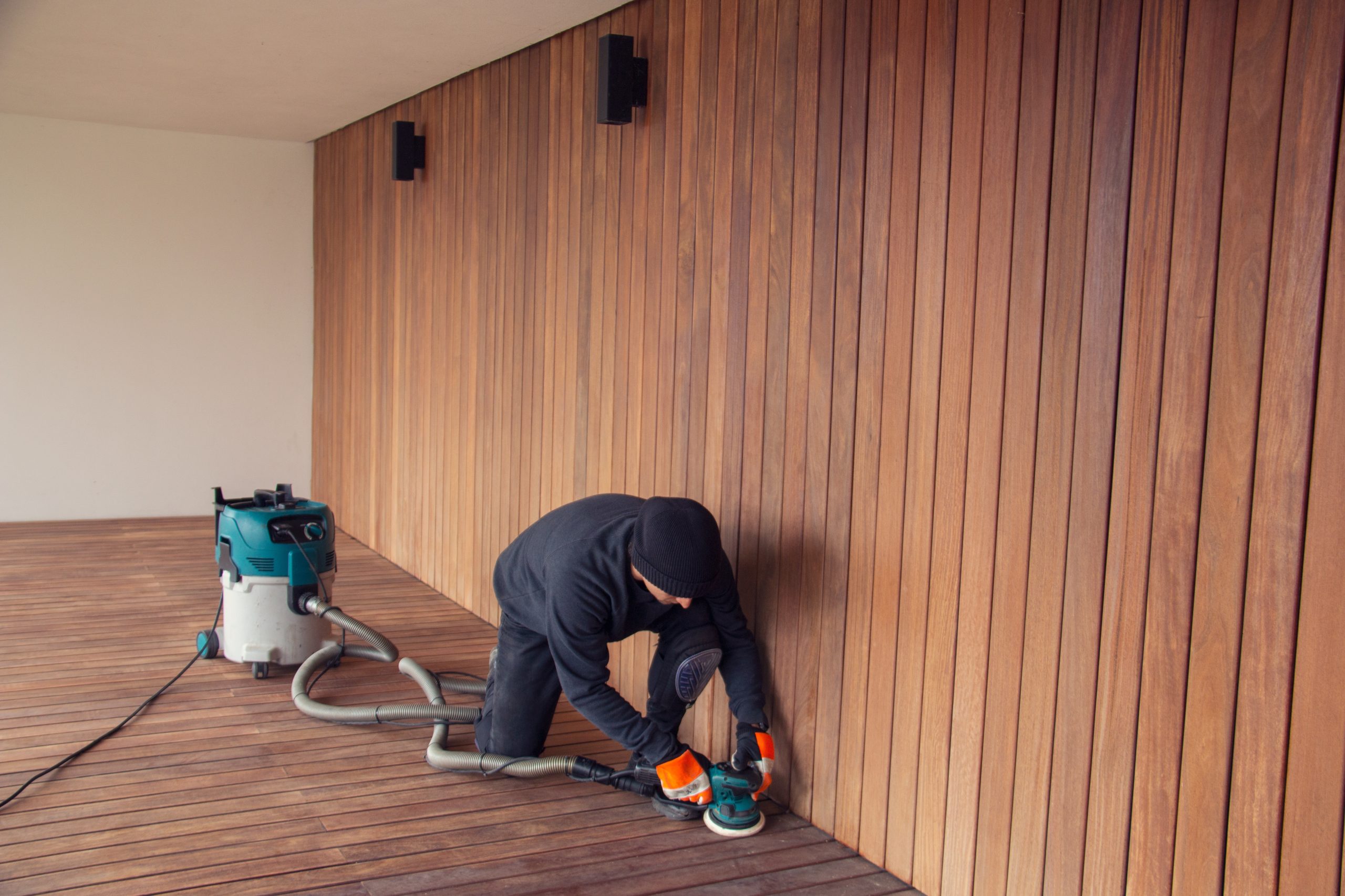 Deck Sanding and Renewal in Catford on a hardwood timber deck floor, with a technician edge-sanding the boards beside a matching vertical timber wall using dust-free equipment.