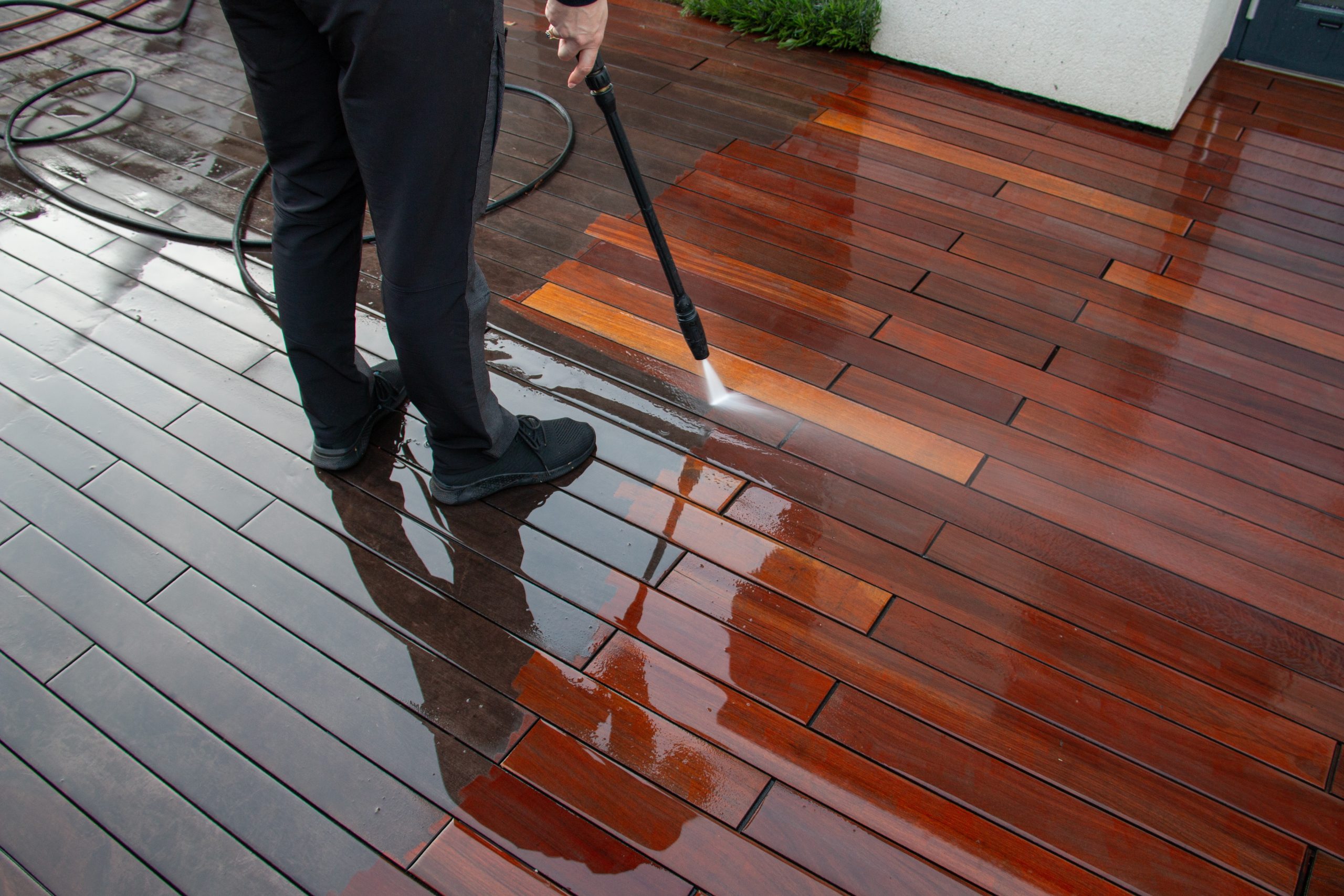 Professional cleaning after Deck Sanding and Renewal in Catford on a glossy hardwood timber garden deck floor, using a pressure washer to rinse the restored boards.