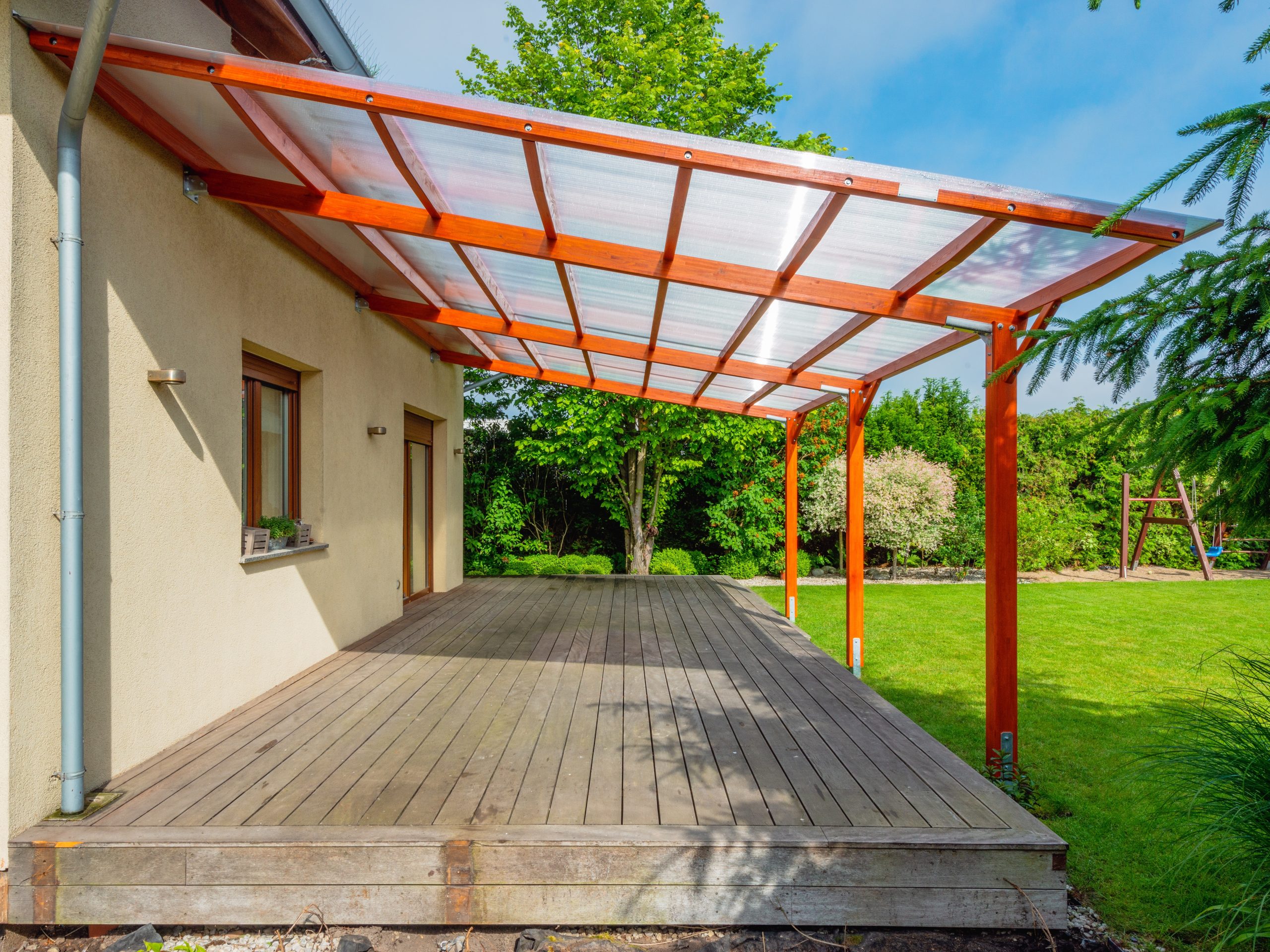 Weathered timber garden patio decking veranda needing Deck Sanding and Renewal in Catford, with a covered wooden terrace overlooking a green lawn.