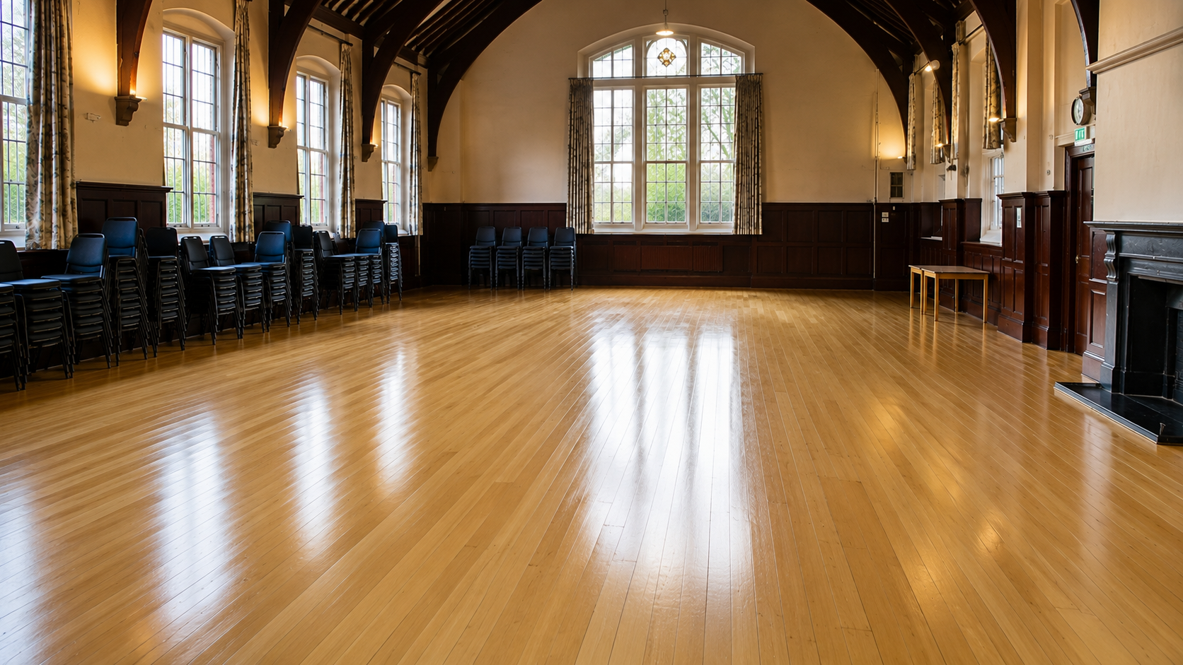 Completed village hall floor sanding and restoration showing a smooth, glossy wooden floor in a large community hall with arched ceiling and stacked chairs